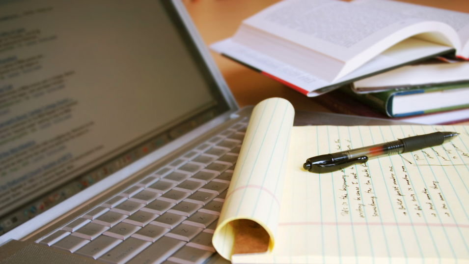 En notesblok med videnskabelige notater, en computer og nogle bøger med opslag i